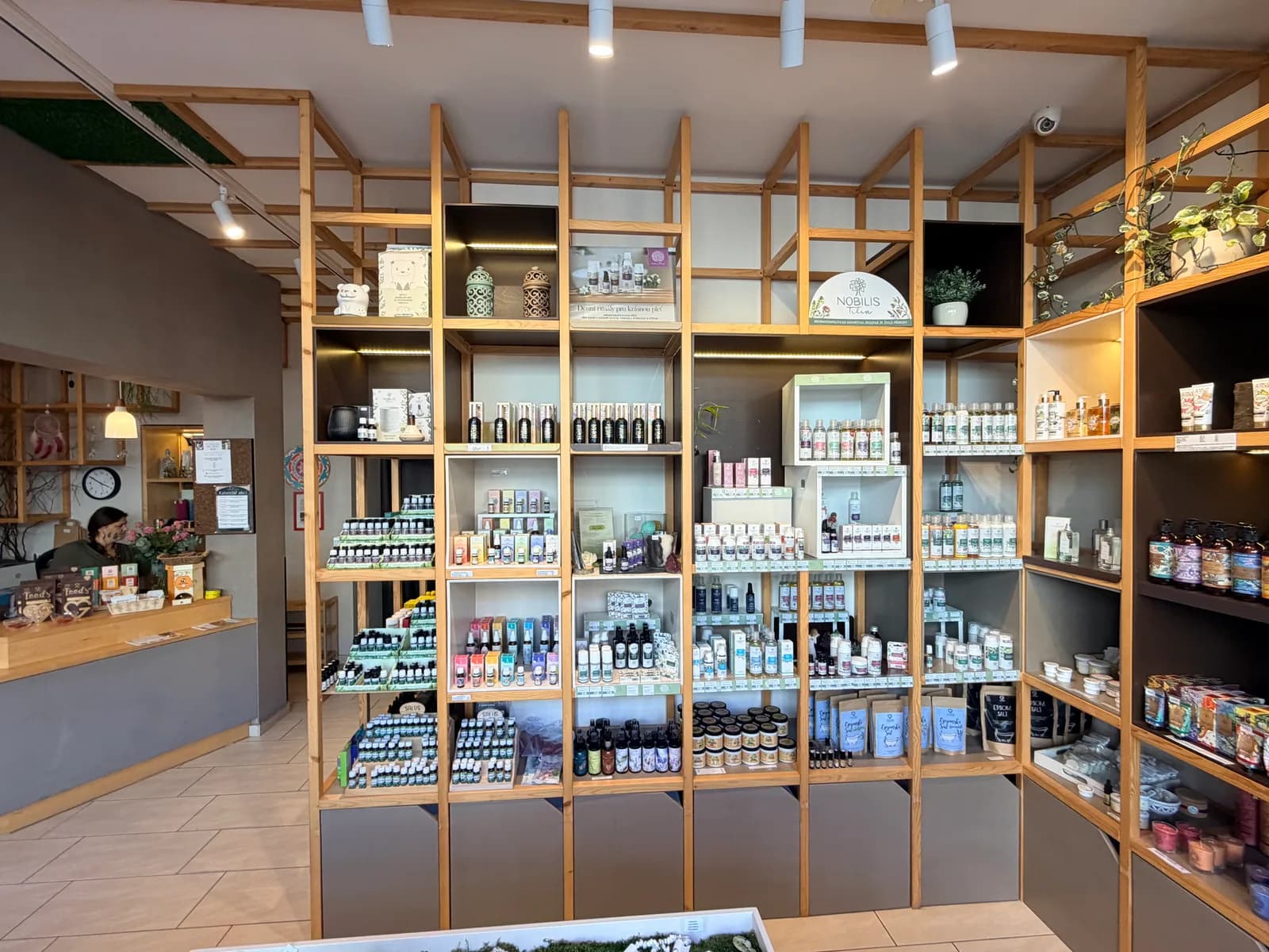 Obsluha u pultu prodejny mezi regály plnými produktů